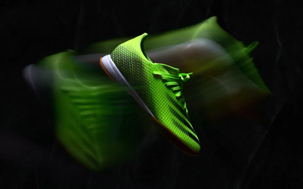 Green indoor soccer shoes with motion effect on a black background