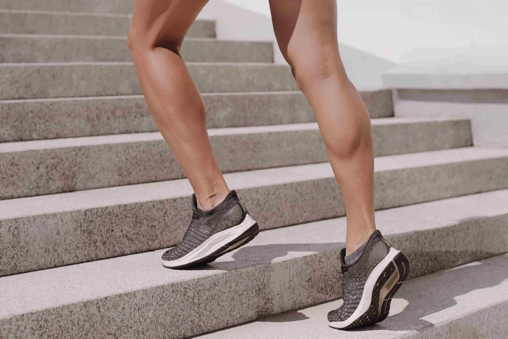 Person wearing running shoes walking up outdoor concrete stairs.