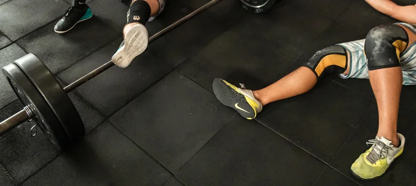 Athletes resting on a gym floor beside a barbell after weightlifting