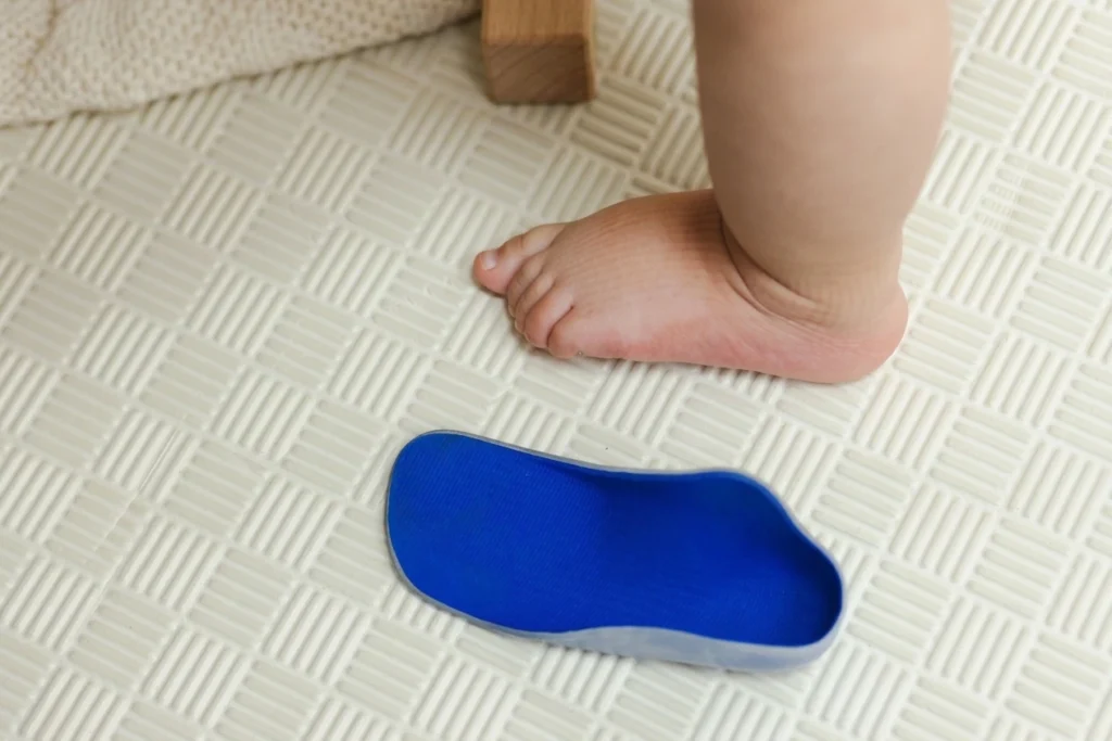 Child barefoot next to a blue orthotic insole